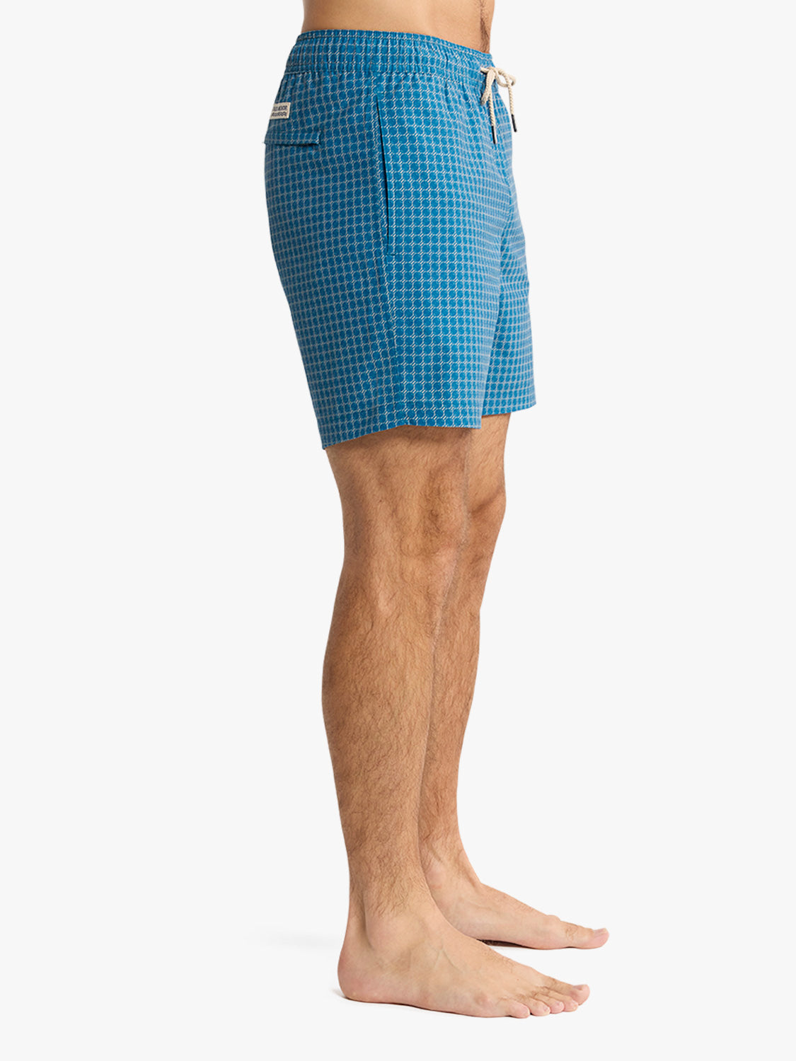 Man wearing teal swim trunks with a geometric dot pattern and drawstring waist.