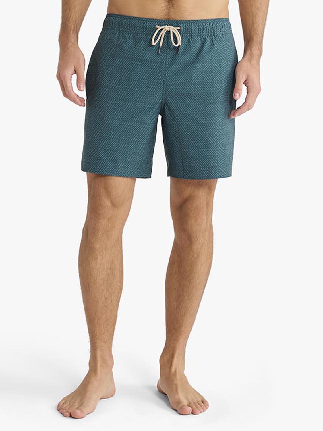 Man wearing teal shibori-patterned swim trunks with a drawstring waistband.