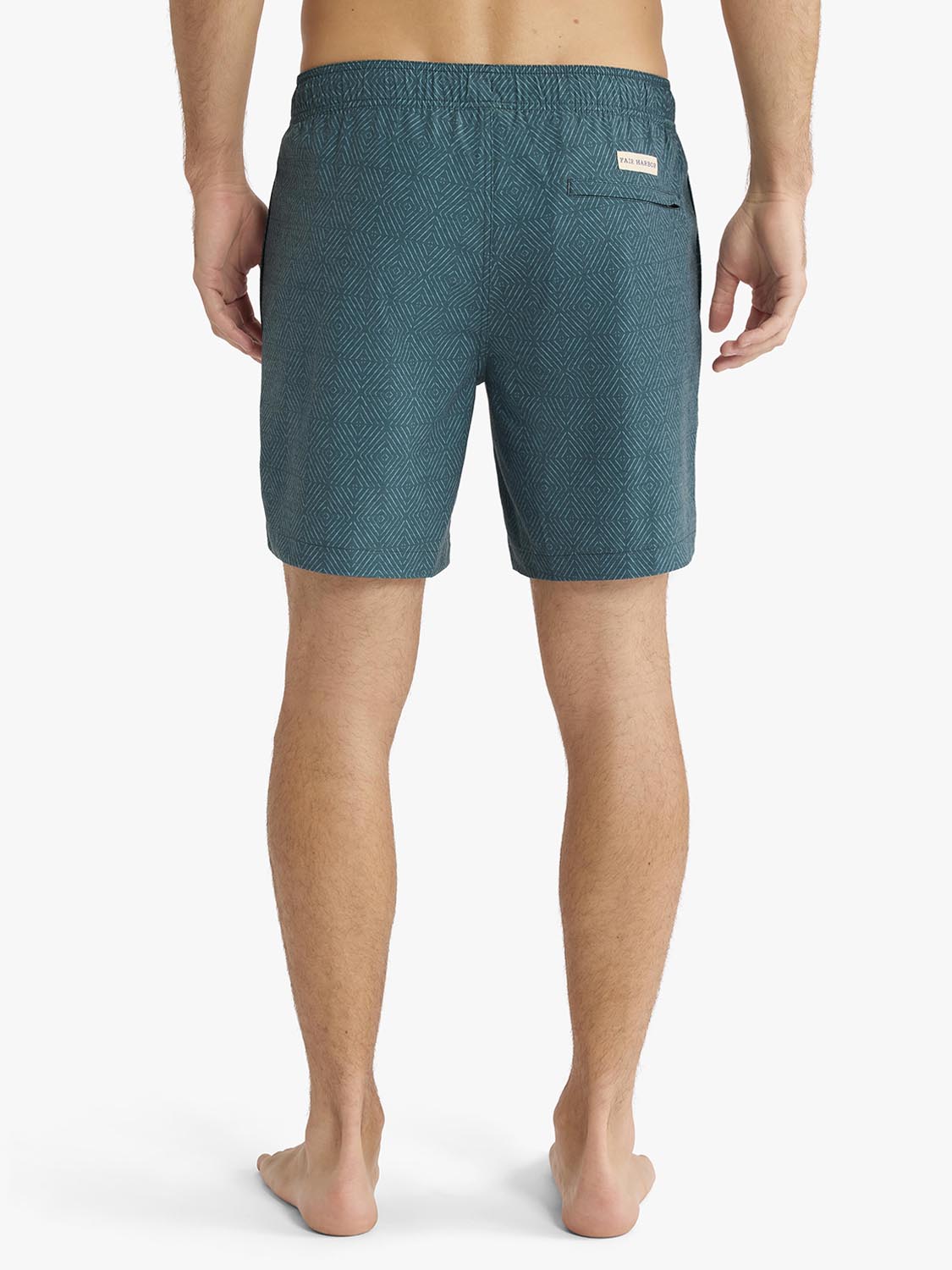 Man wearing teal shibori-patterned swim trunks with geometric diamond design viewed from behind.