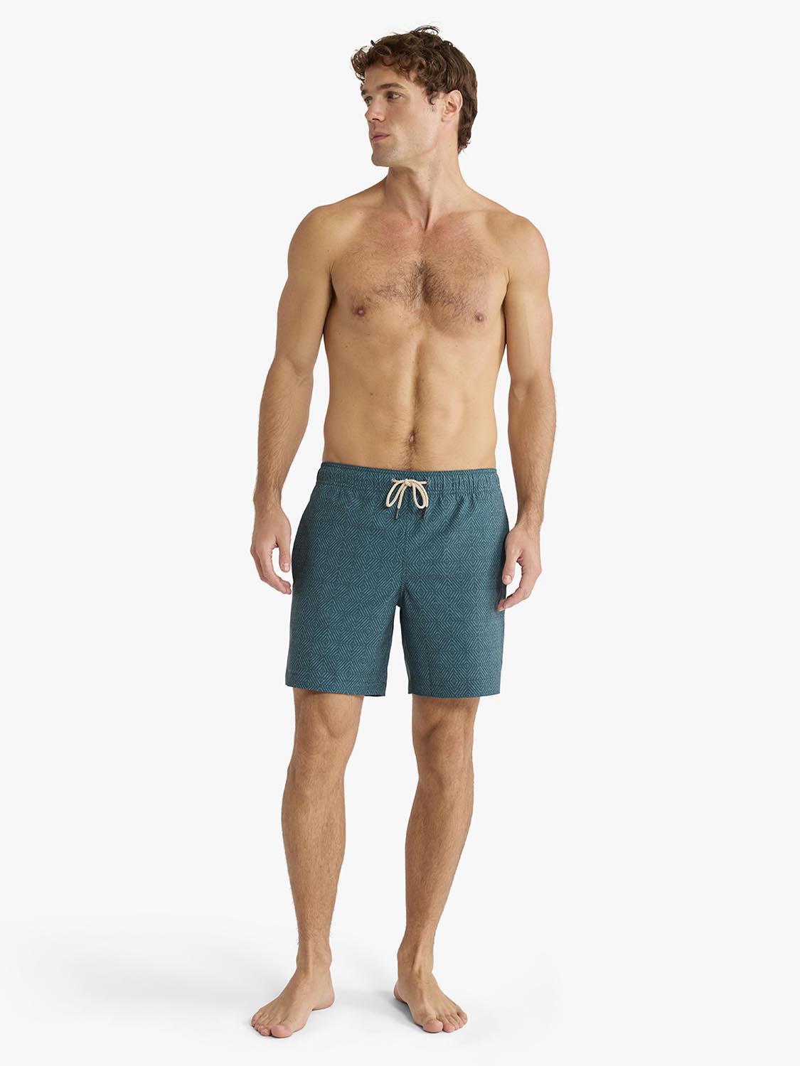 Man wearing green shibori patterned swim trunks with a drawstring waist standing against white background.