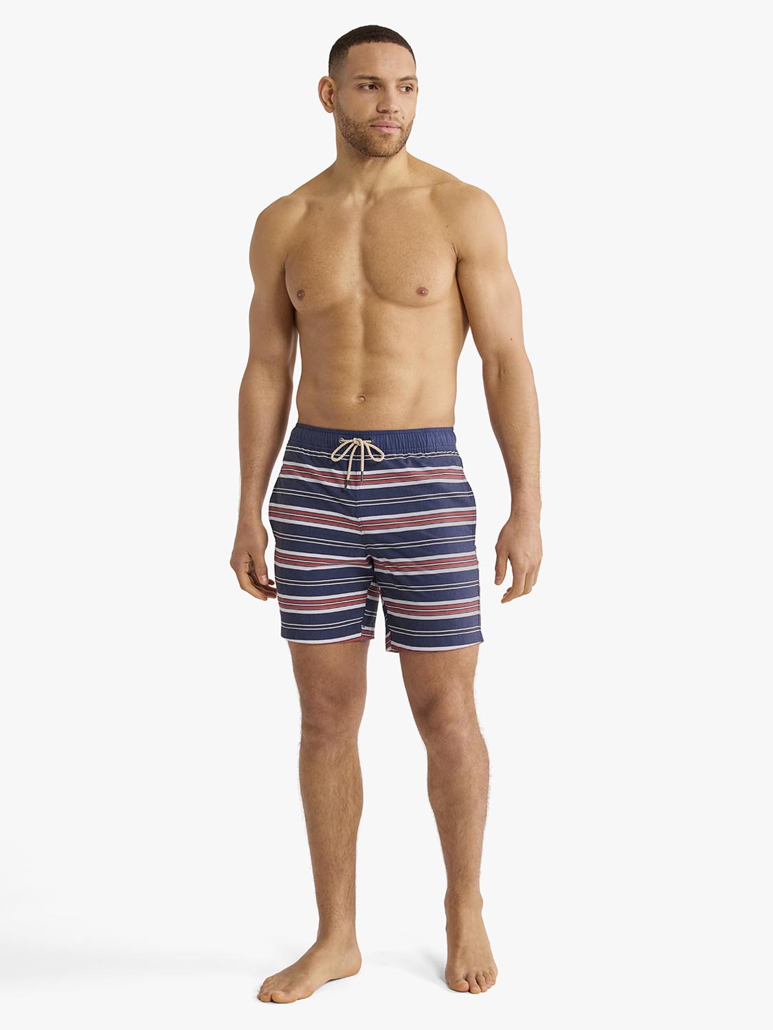 Man wearing navy swim trunks with red and white horizontal stripes and drawstring waist.