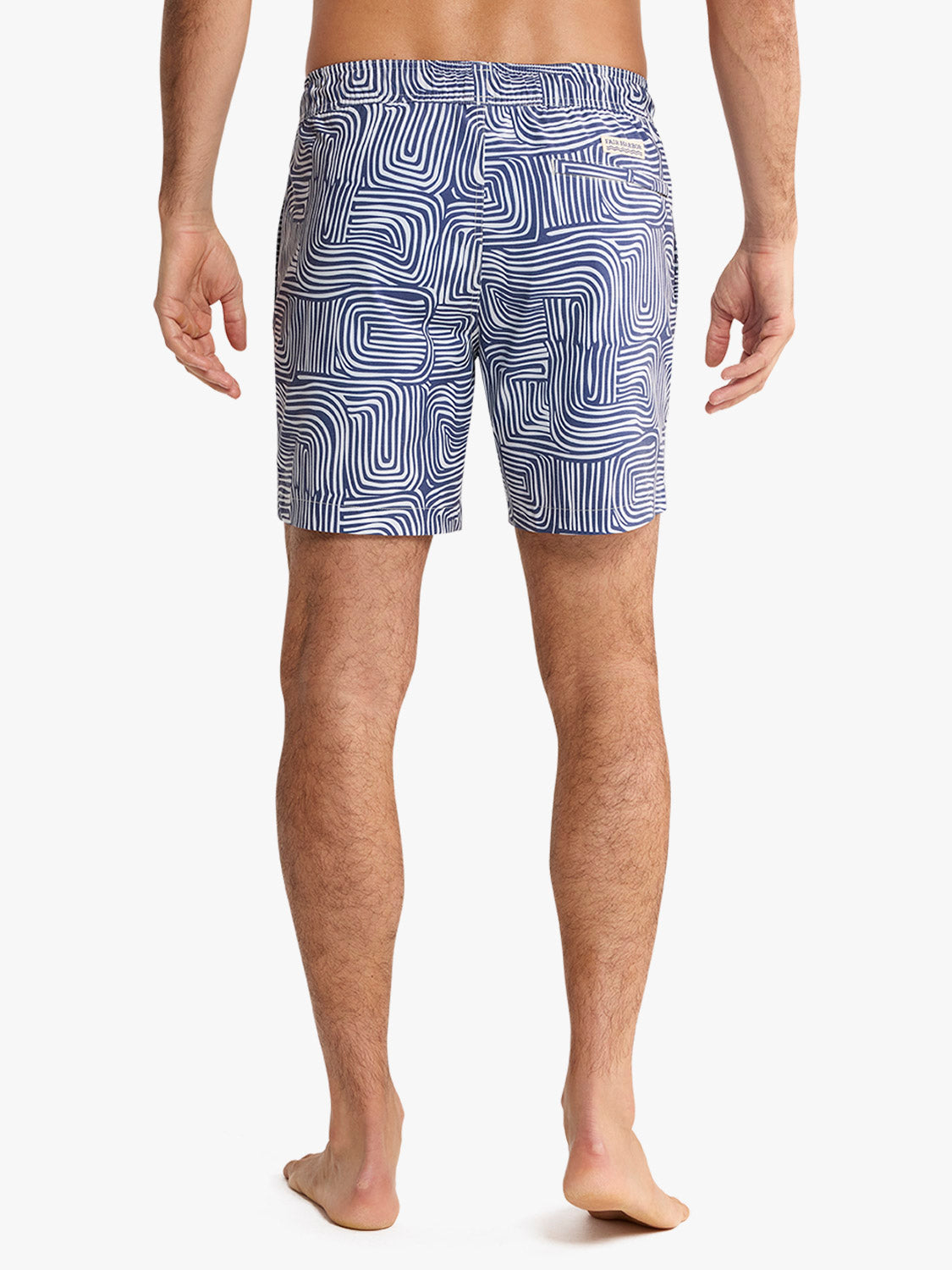 Man wearing navy and white wavy patterned swim trunks standing against a white background.