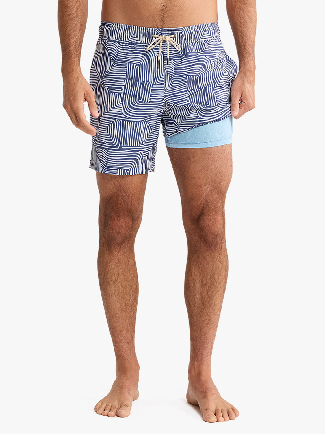 Man wearing navy and white wavy patterned swim trunk with light blue compression shorts underneath.