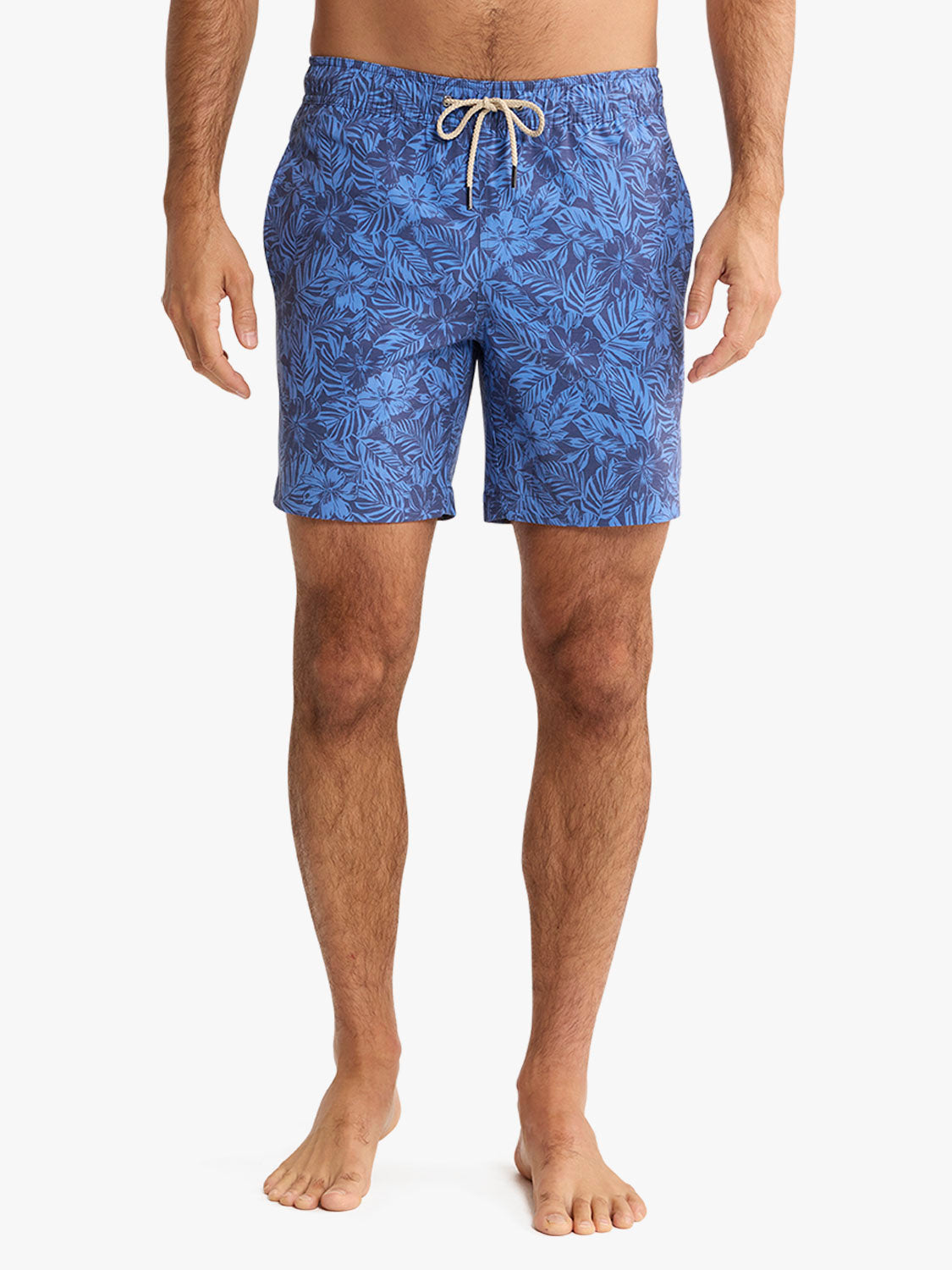 Man wearing blue swim shorts with a dark leaf pattern and tan drawstring waistband.