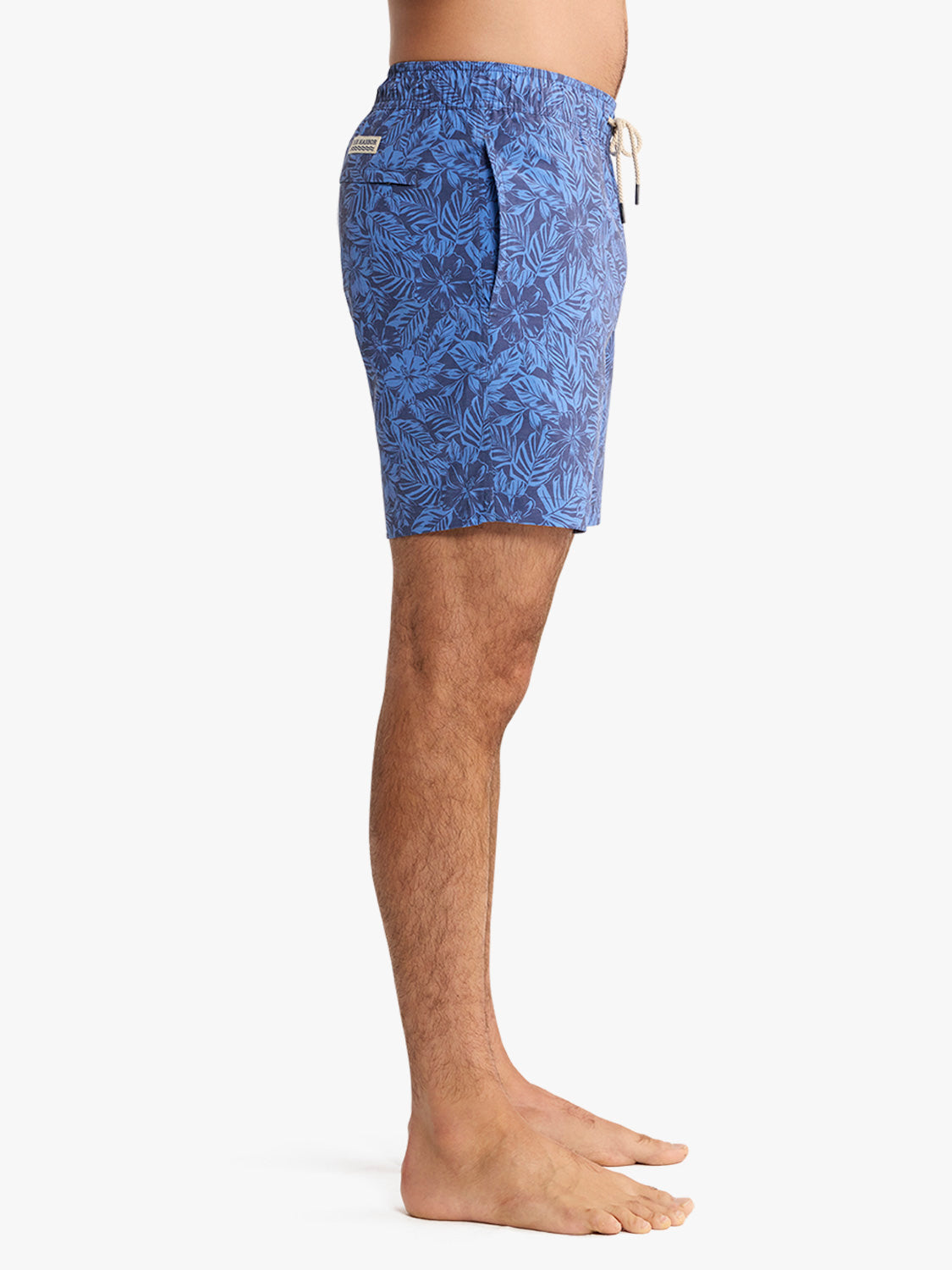 Man wearing blue swim trunk with dark leaf pattern and drawstring waist detail.