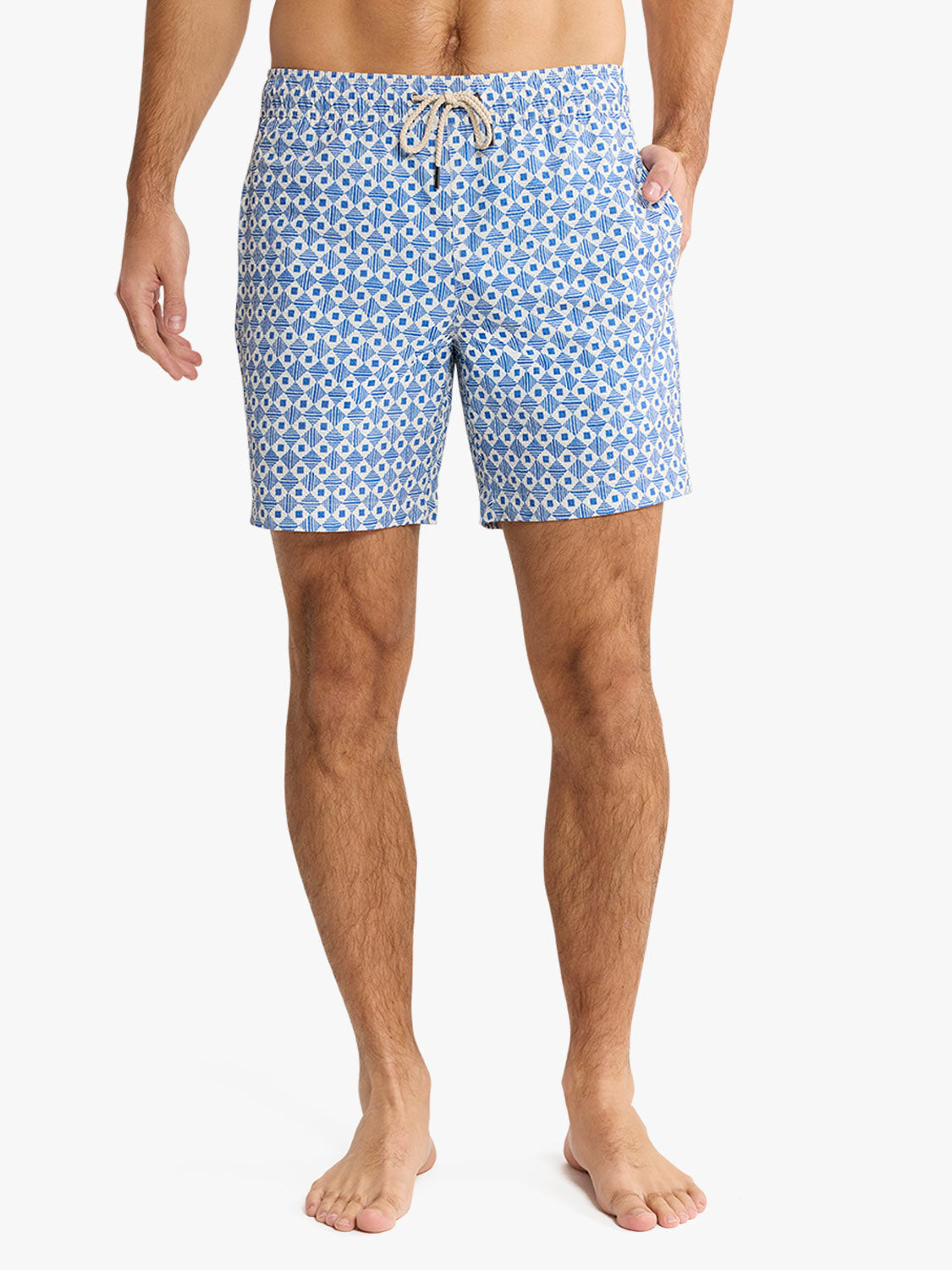 Man wearing blue and white geometric tile-patterned swim shorts with drawstring waist and side pockets.