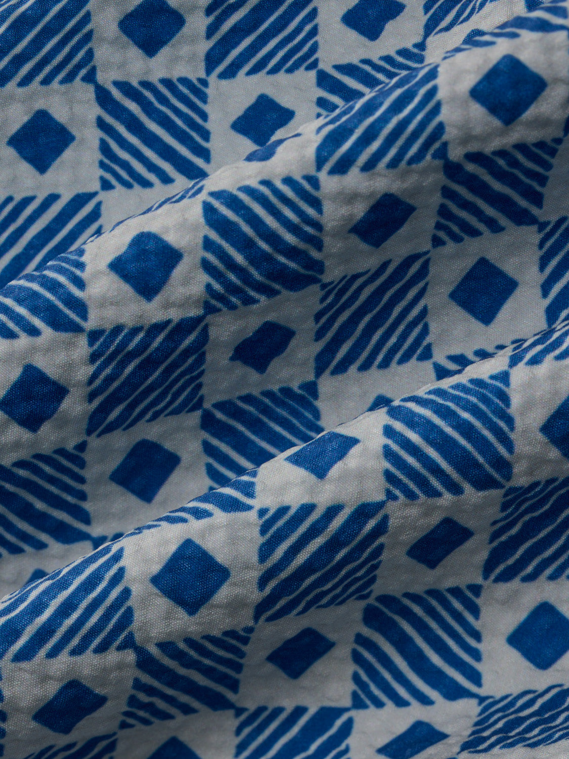 Blue and white seersucker fabric with diamond and striped tile pattern design.