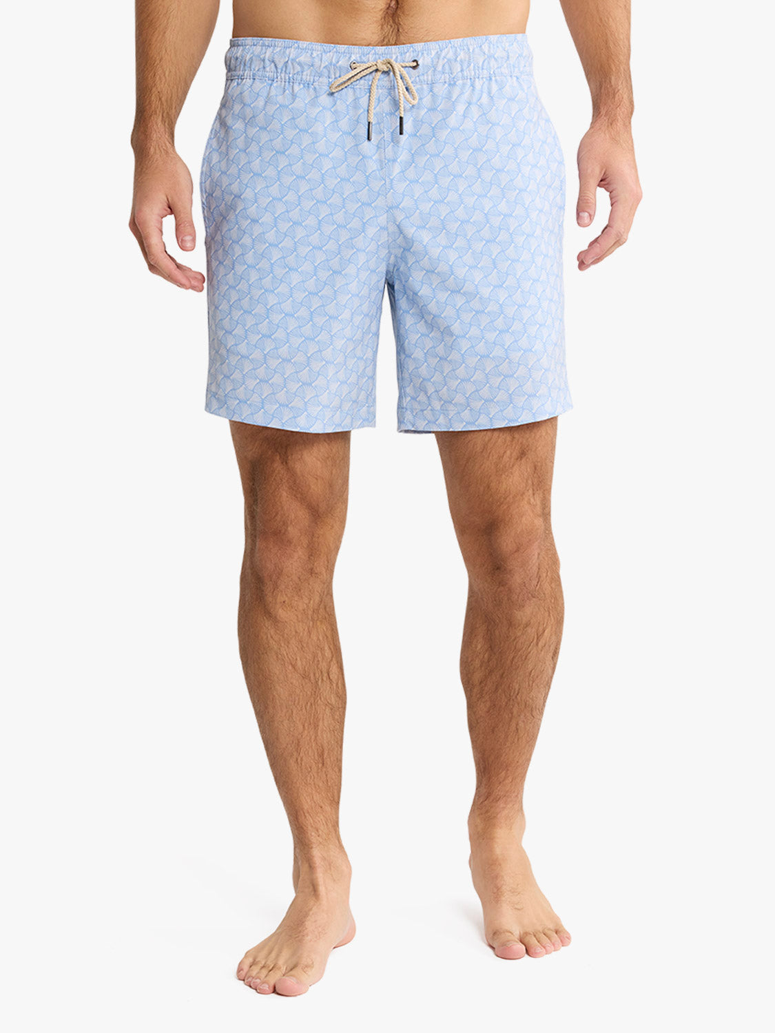 Man wearing sky blue swim trunks with an all-over shell pattern and tan drawstring.