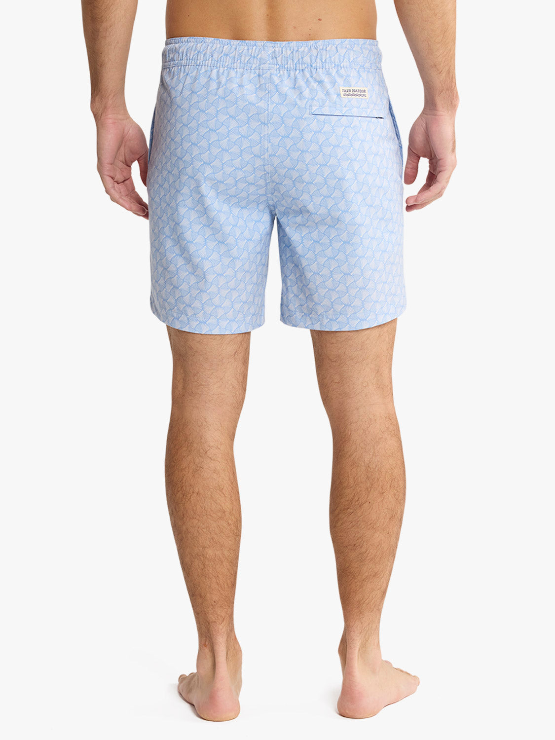 Sky blue swim trunks with an all-over shell pattern and back pocket detail displayed on a man.