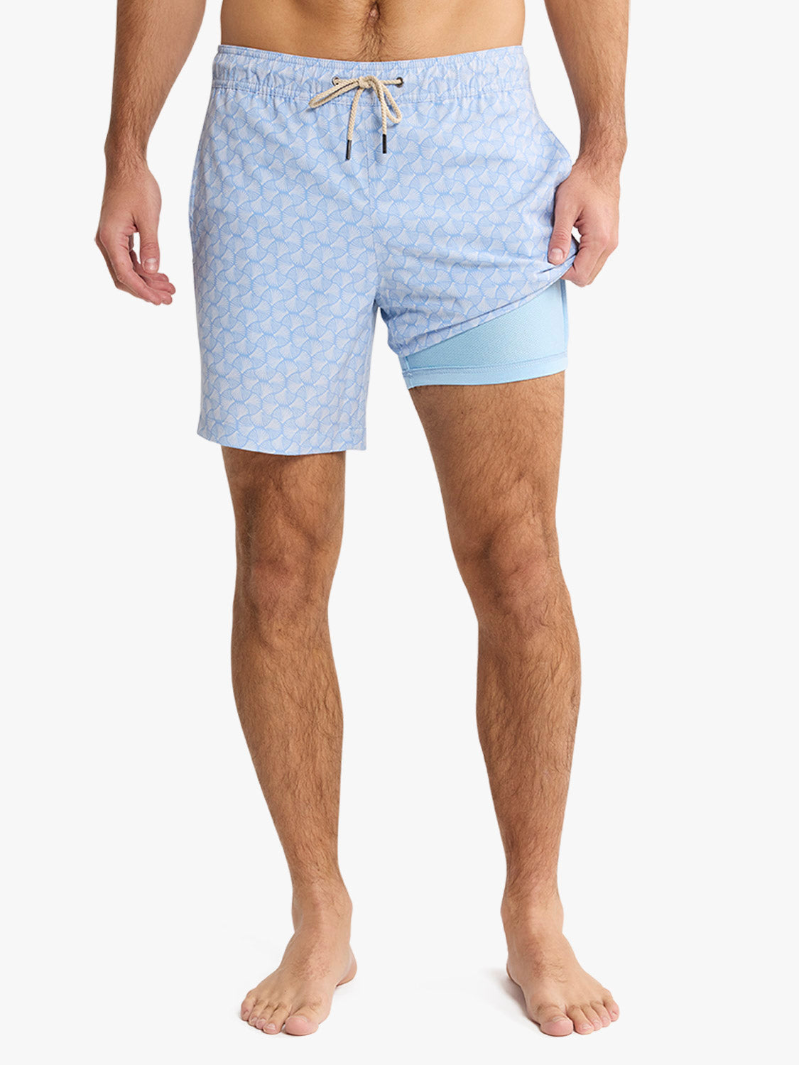 Man wearing sky blue swim trunks with shell pattern and built-in inner shorts.