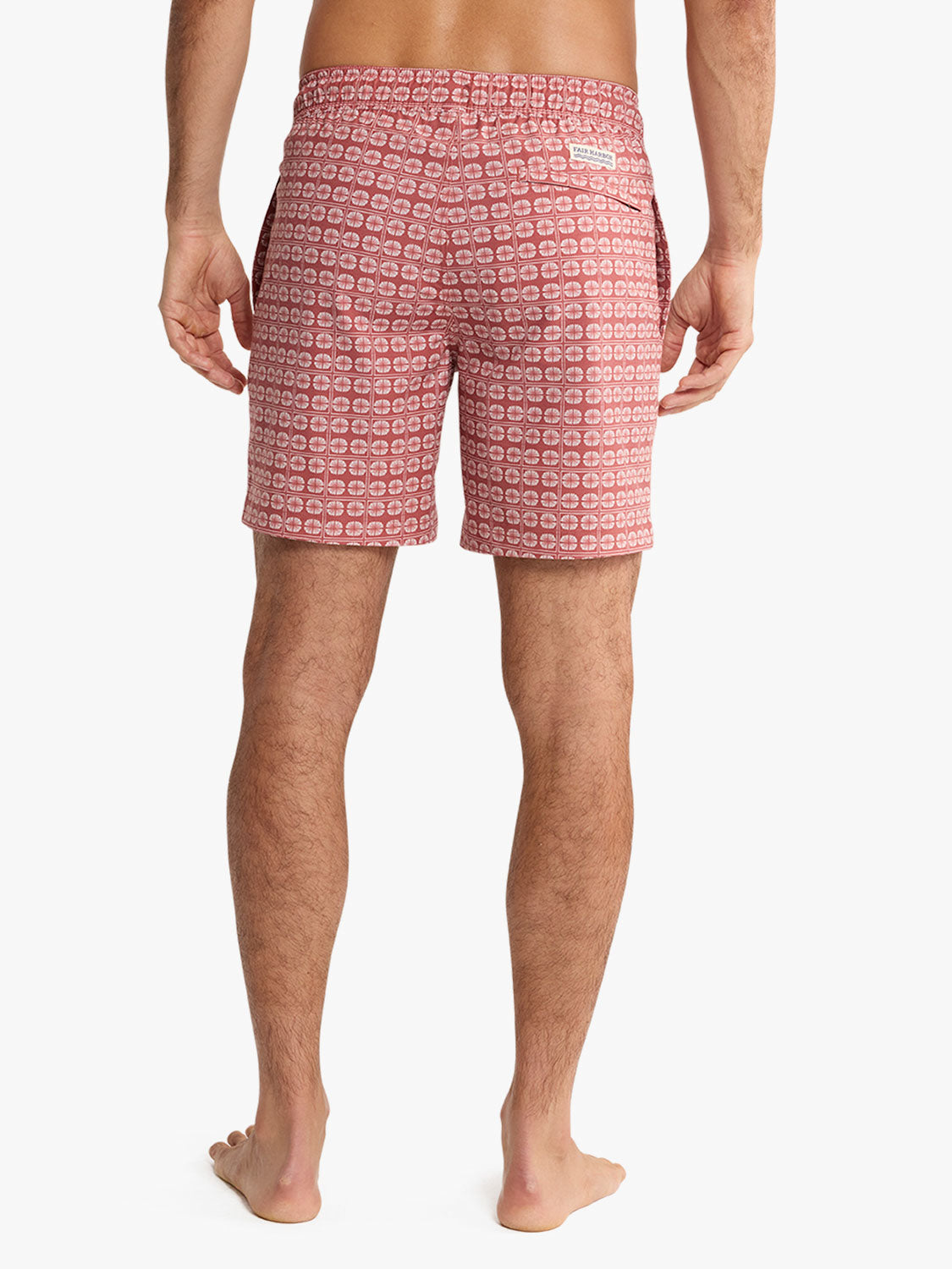 Man wearing red patterned swim trunks with geometric sand dollar design shown from behind.