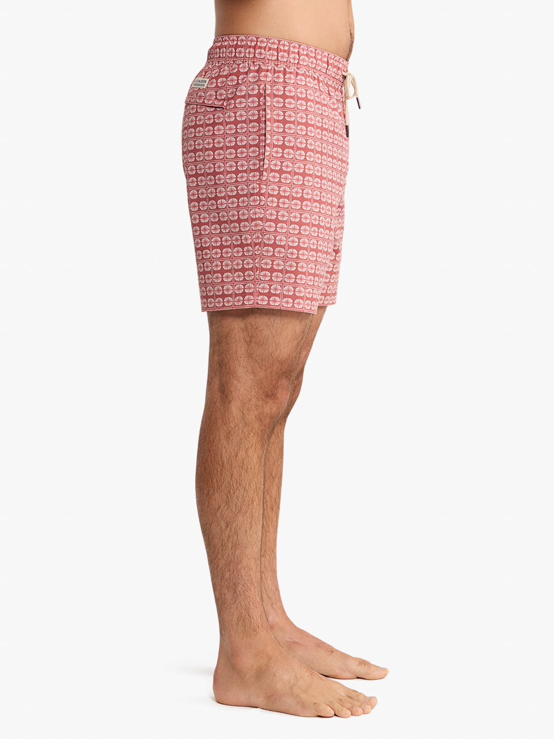 Man wearing red patterned swim trunk with drawstring waist and geometric circle print.