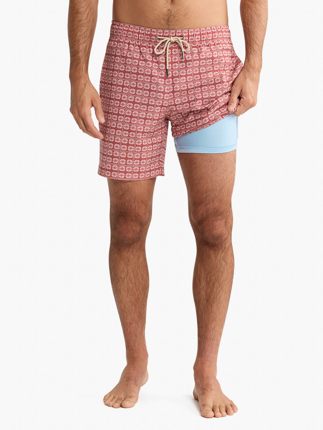 Man wearing redstone pink swim trunks with sand dollar pattern and light blue compression shorts underneath.