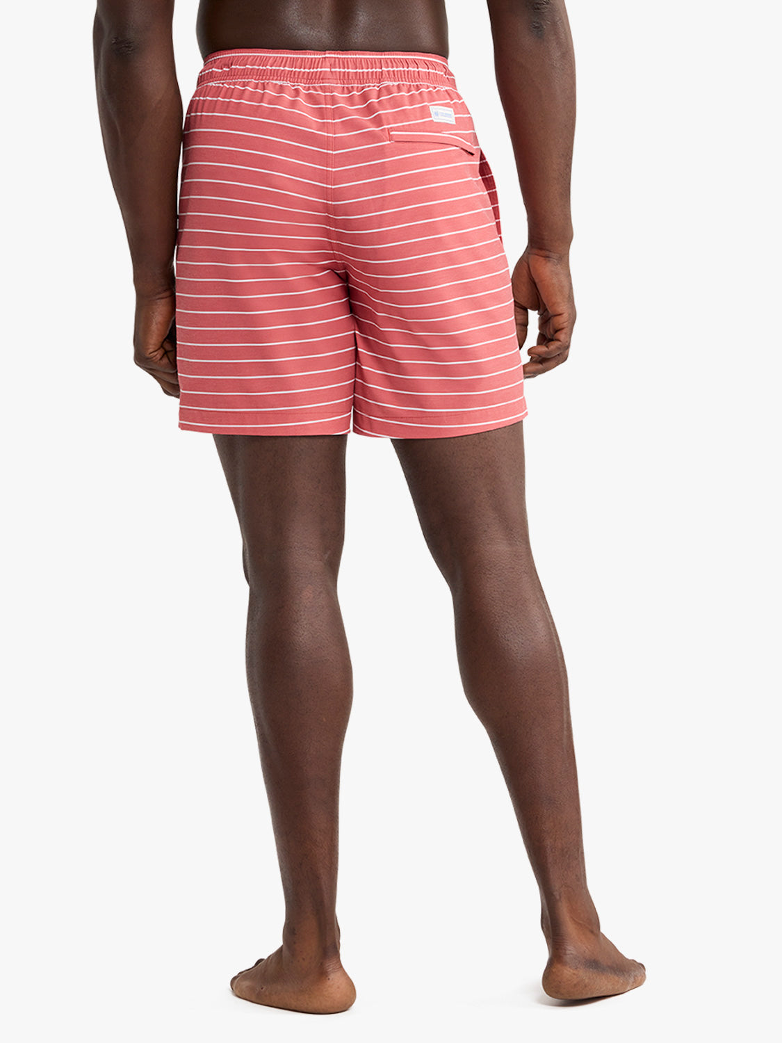 Man wearing red and white striped swim trunks with elastic waistband and side pockets.