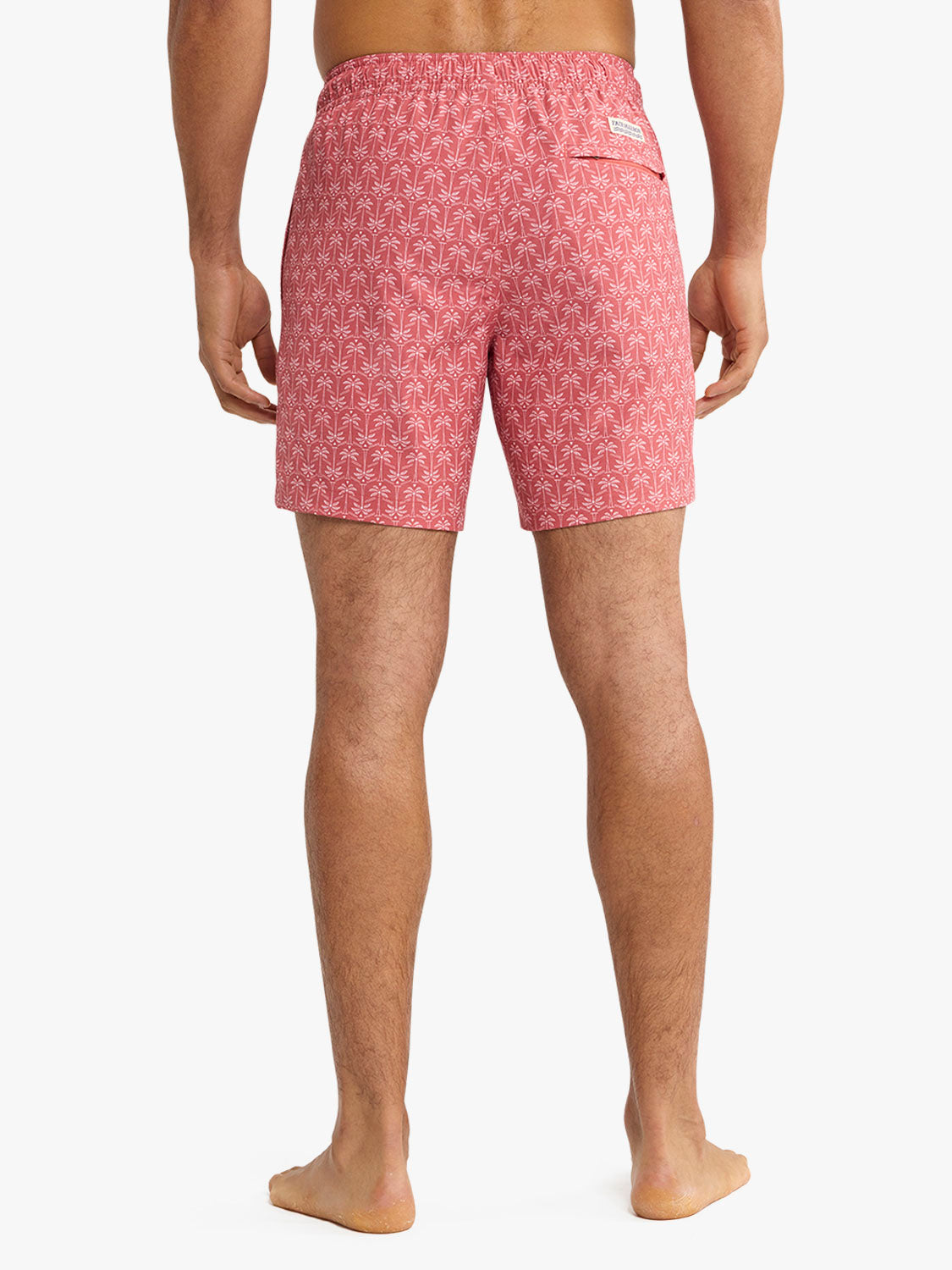 Man wearing red swim trunks with white palm leaf pattern, shown from behind at waist to feet.