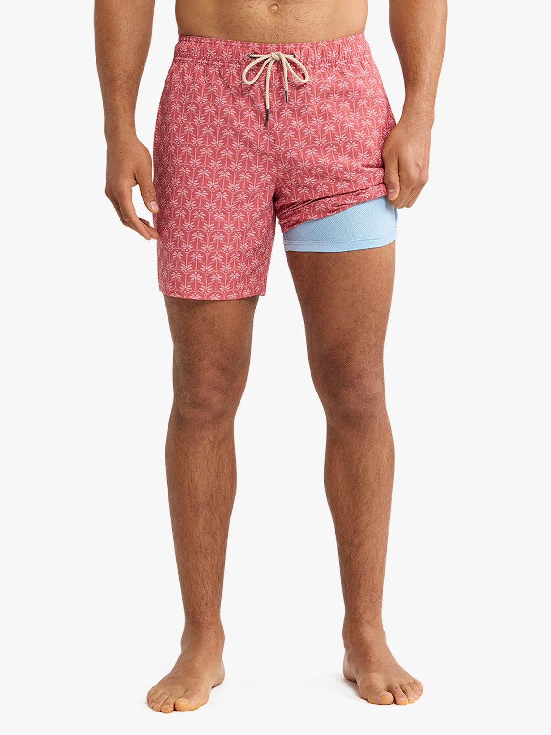 Man wearing red swim trunks with geometric palm pattern and light blue liner shorts.