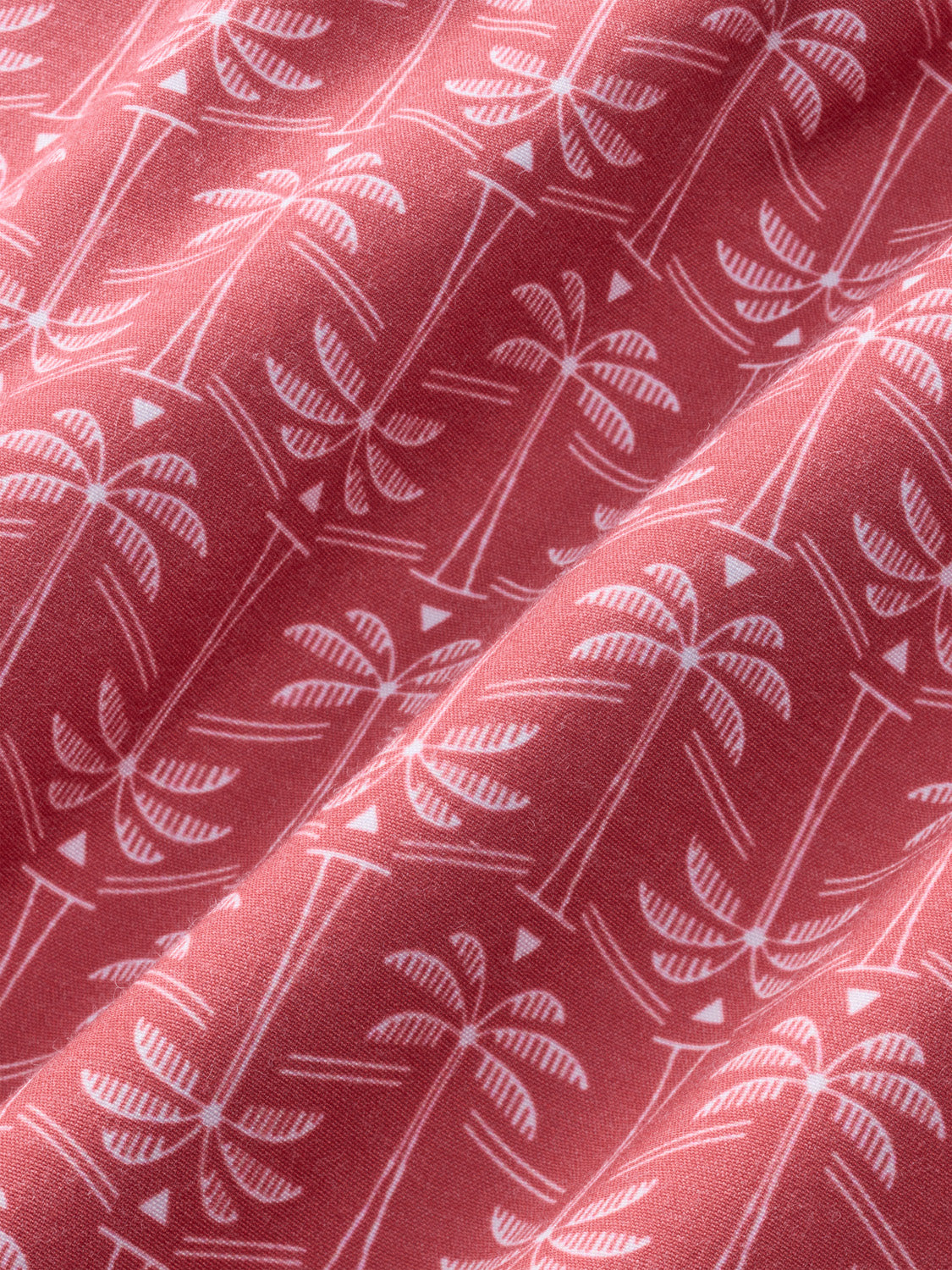 Red fabric with white palm tree and geometric pattern throughout showing textured weave detail.