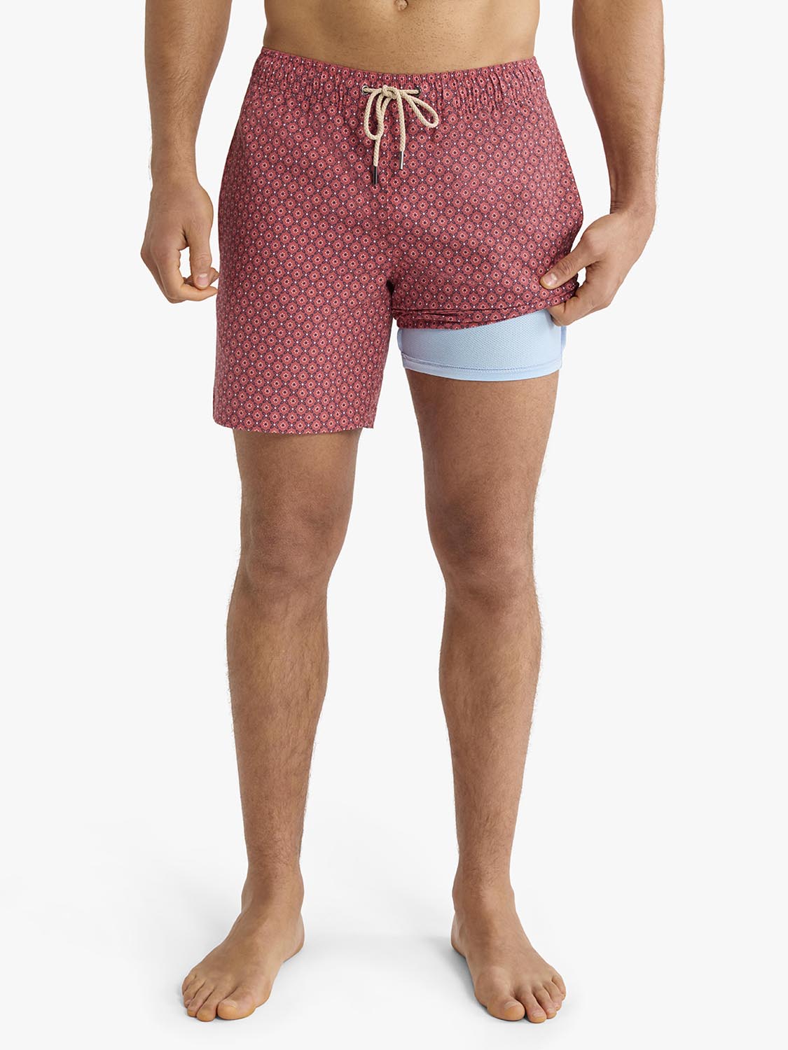 Man wearing red bandana patterned swim trunks with light blue undergarment shorts visible.