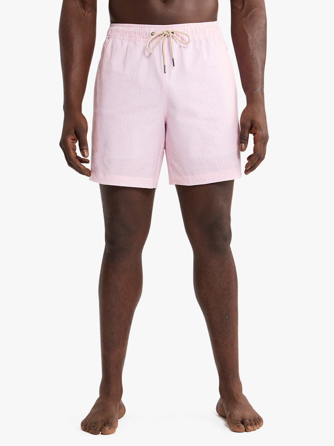 Man wearing light pink seersucker swim trunks with drawstring waist and vertical texture pattern.