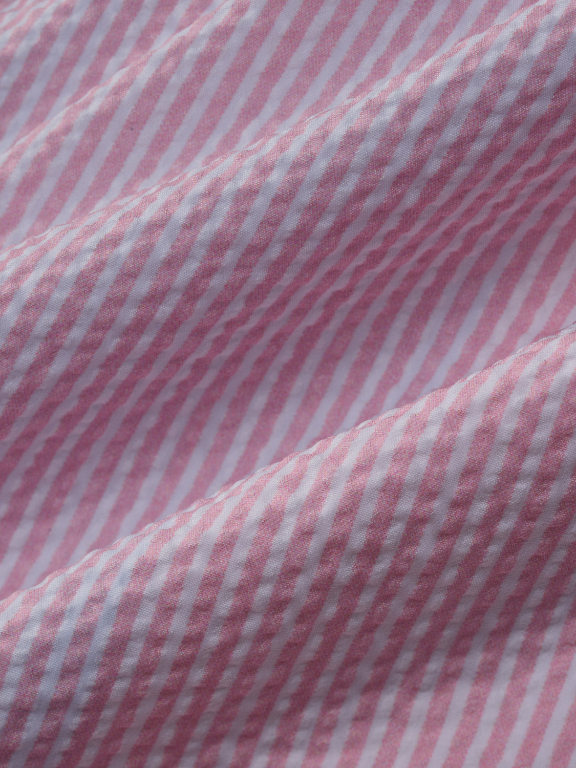 Pink and white seersucker fabric with vertical stripes showing textured weave pattern detail.