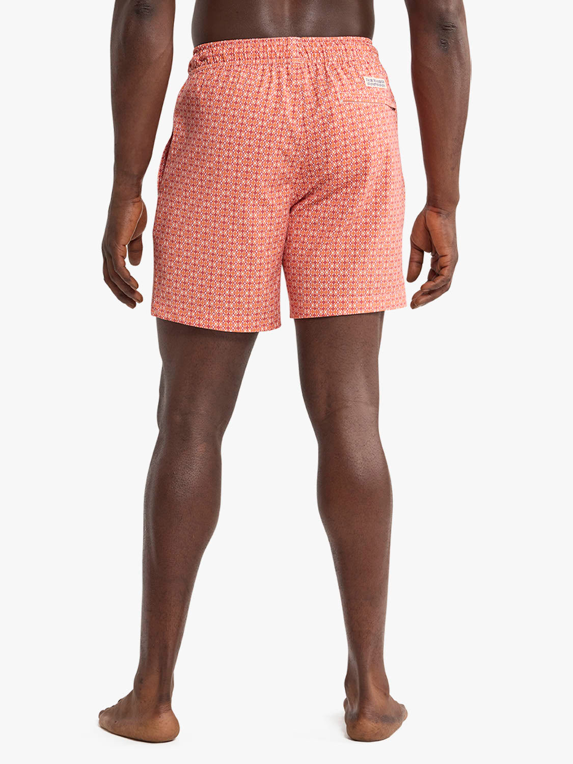 Man wearing tangerine swim trunks with small geometric pattern, photographed from behind.