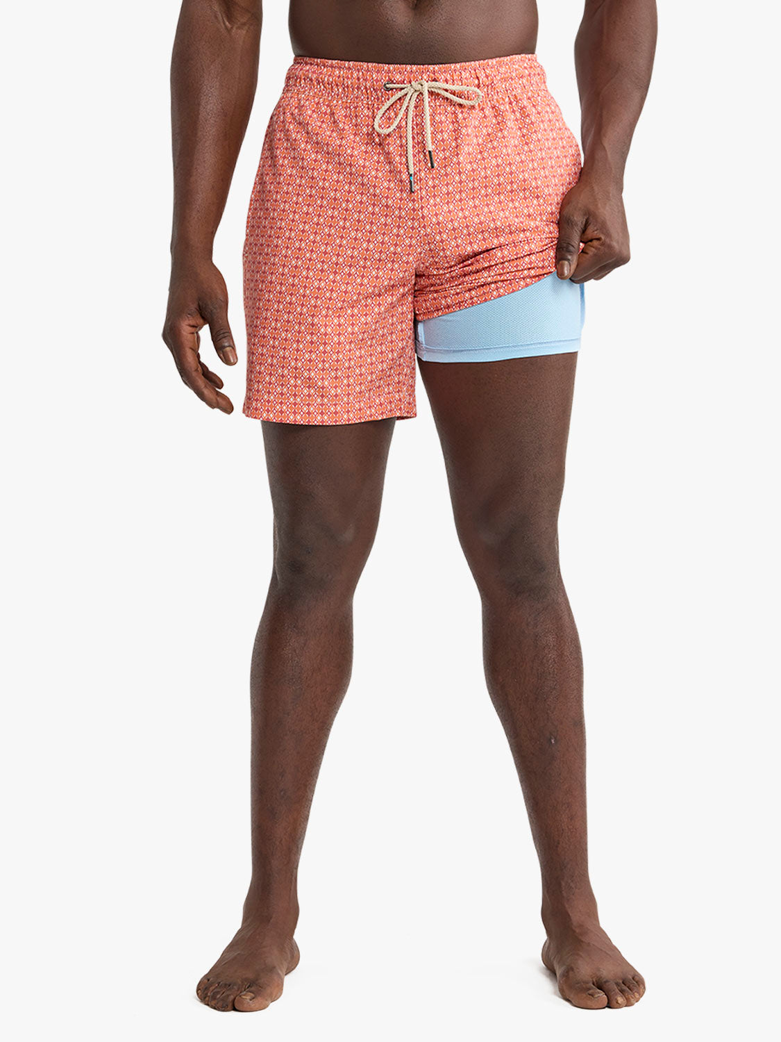 Man wearing tangerine geometric patterned swim trunk with light blue compression liner underneath.