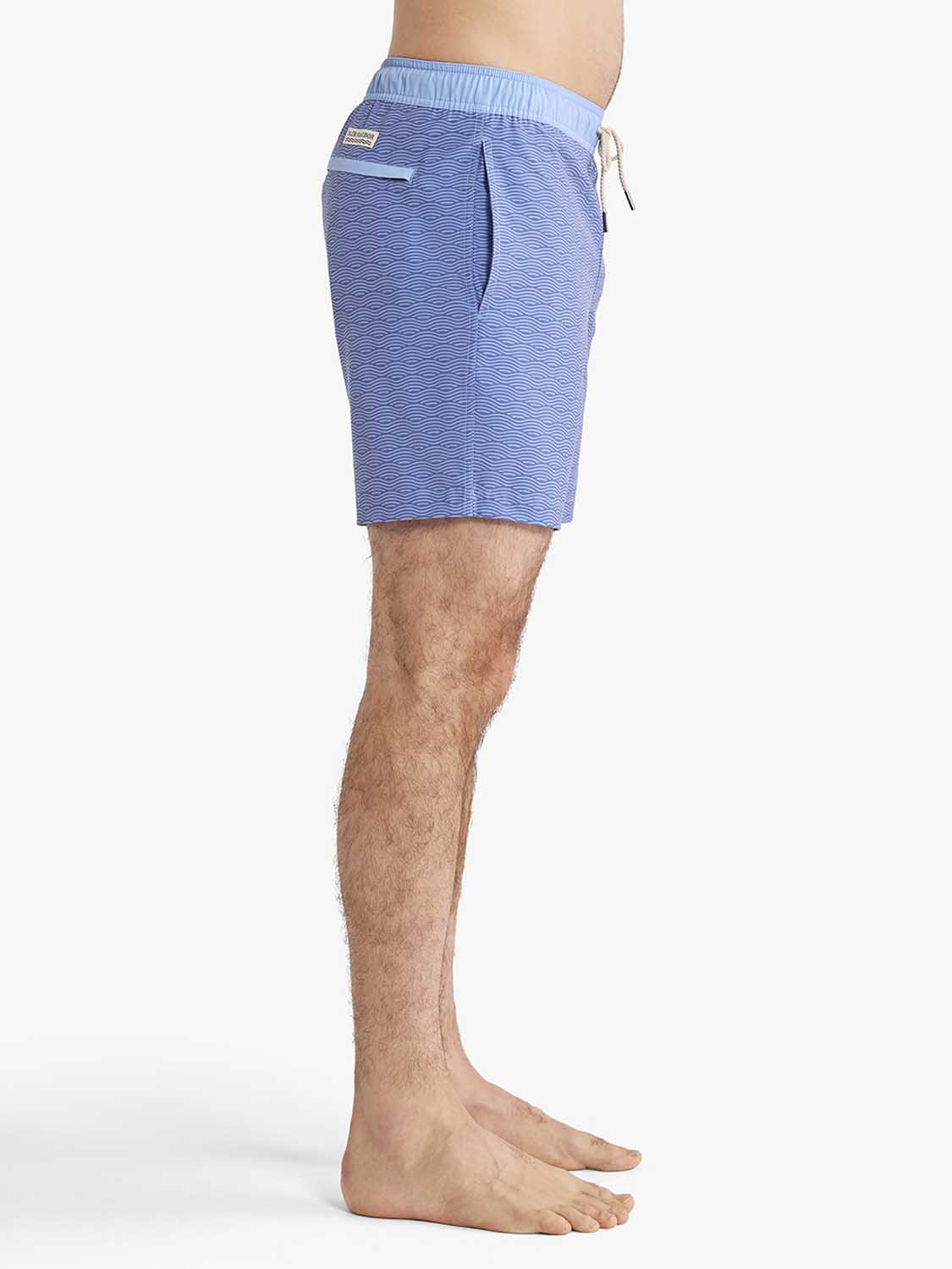 Blue textured swim trunks with drawstring waist and patch pocket worn by man on white background.
