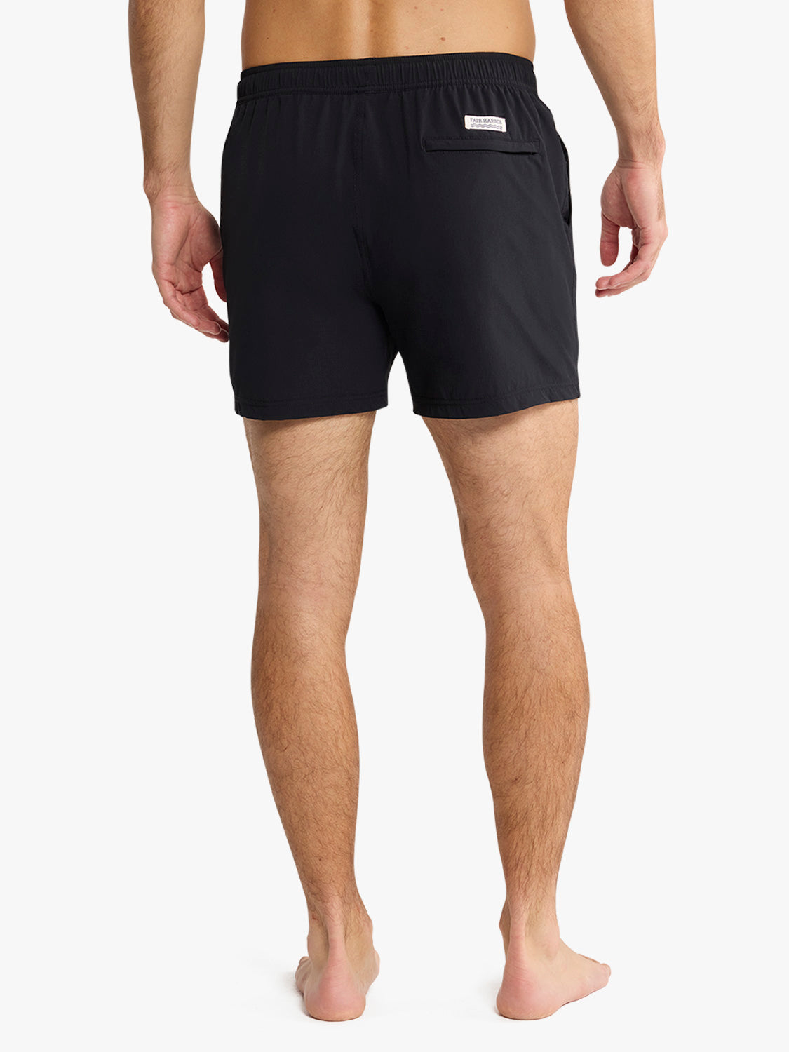 Man wearing black swim trunks with elasticated waist and back pocket viewed from behind.