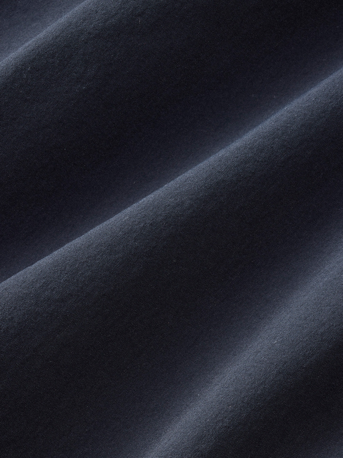 Close-up detail of black fabric with diagonal folds and textured weave pattern throughout.