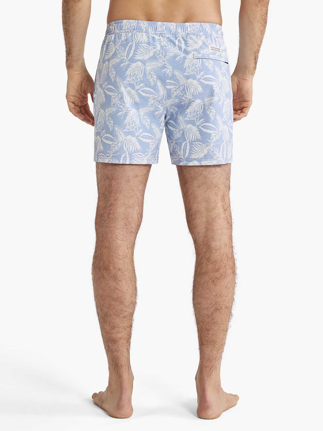 Man wearing sky blue swim trunks with white leaf pattern shown from behind.