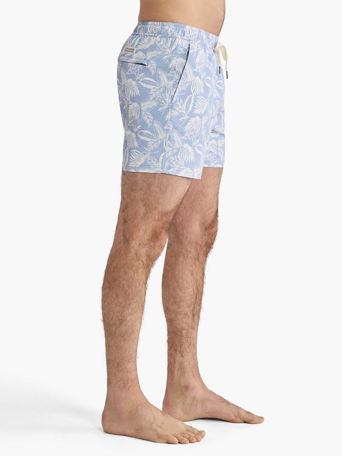 Sky blue swim trunks with cream leaf pattern and elastic waistband displayed on male model.
