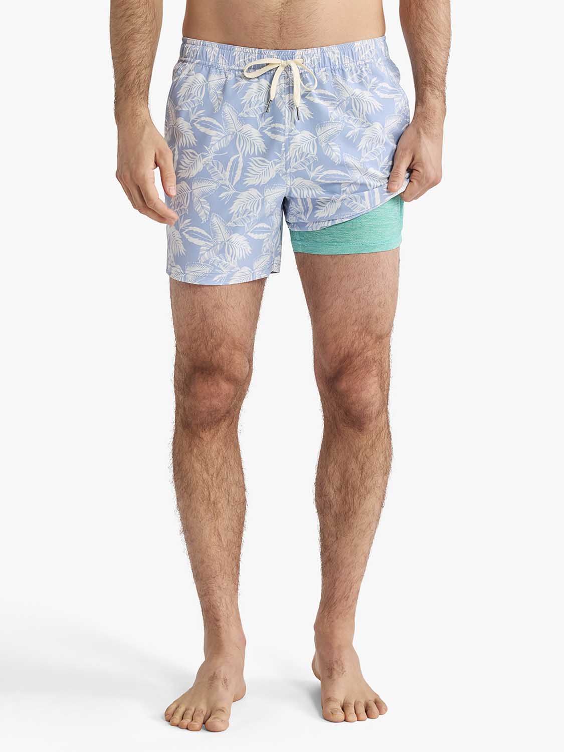 Man wearing sky blue swim trunks with white leaf pattern and green compression shorts underneath.