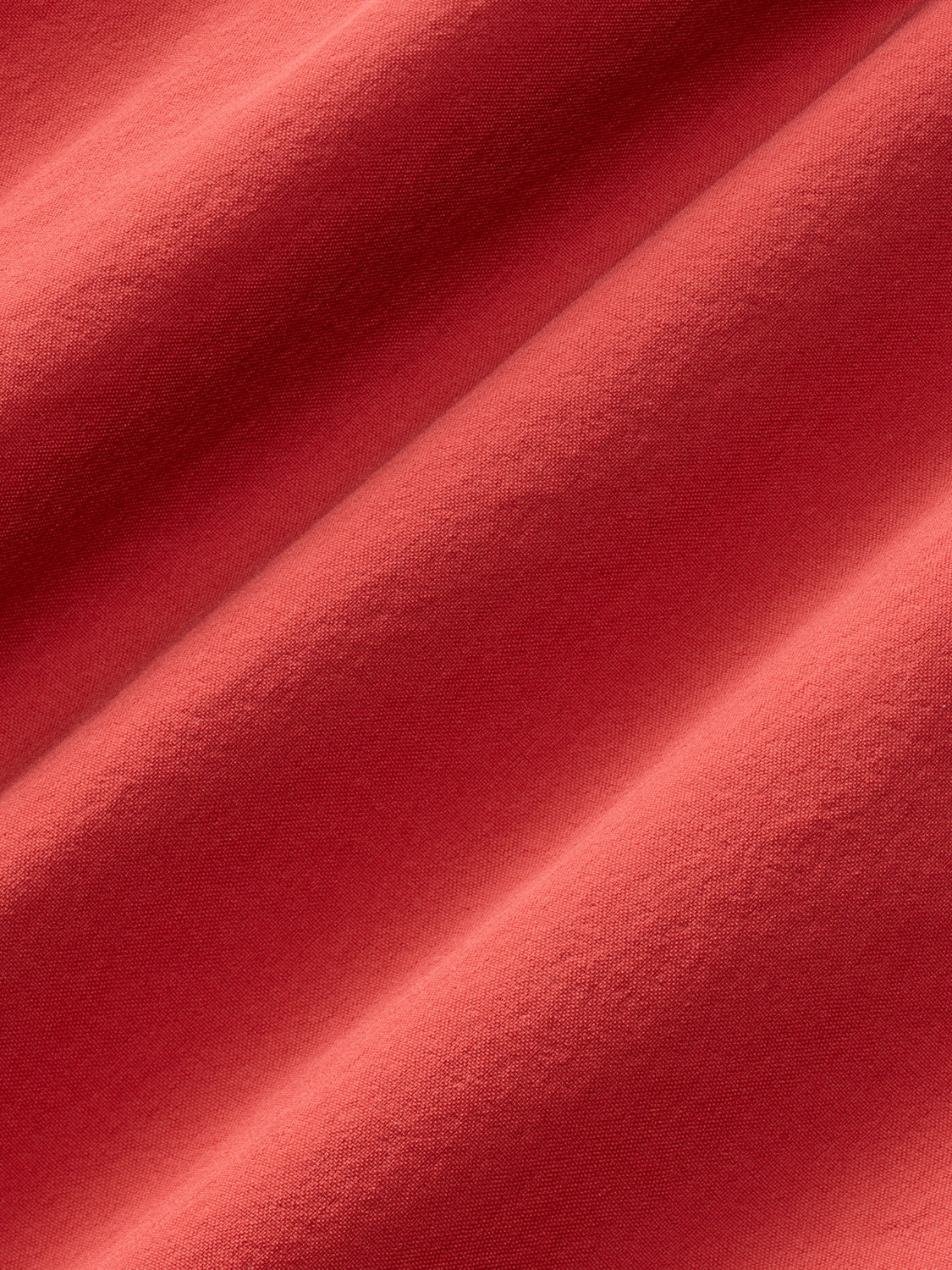 Close-up of baked apple red textured fabric with diagonal folds and shadows.