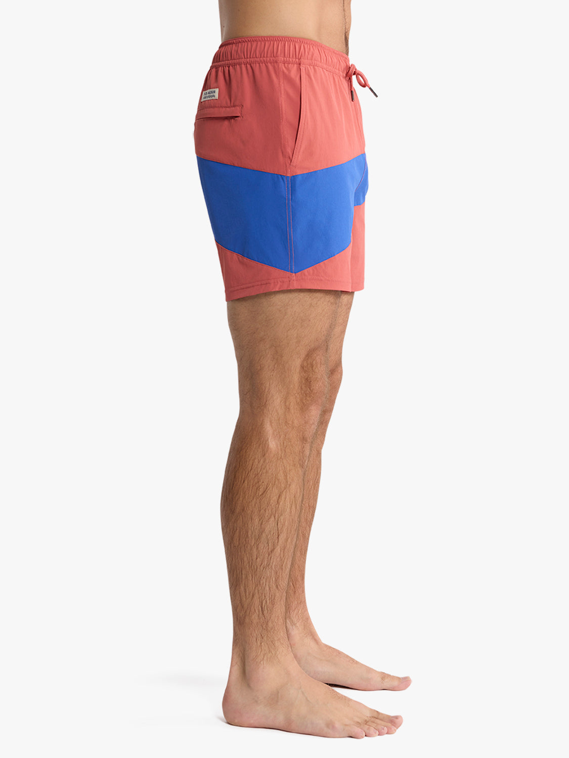 Man wearing red and blue colorblock swim trunk with drawstring waist and side pocket detail.