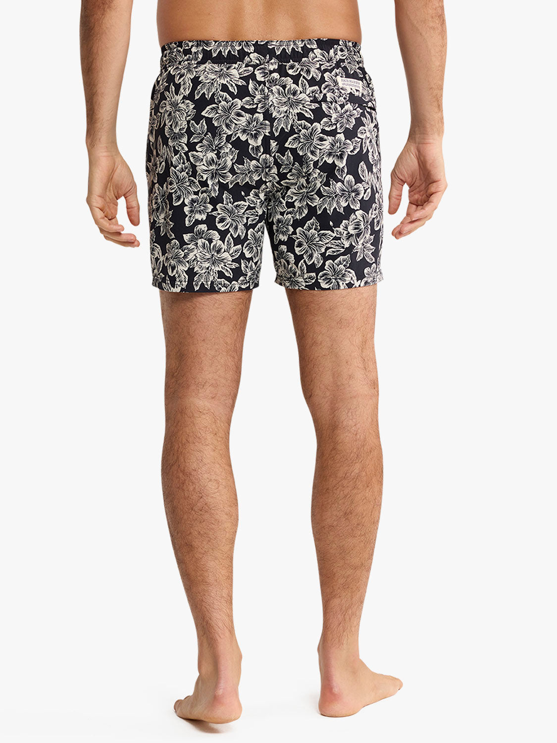 Man wearing black swim trunks with white hibiscus floral print pattern throughout.