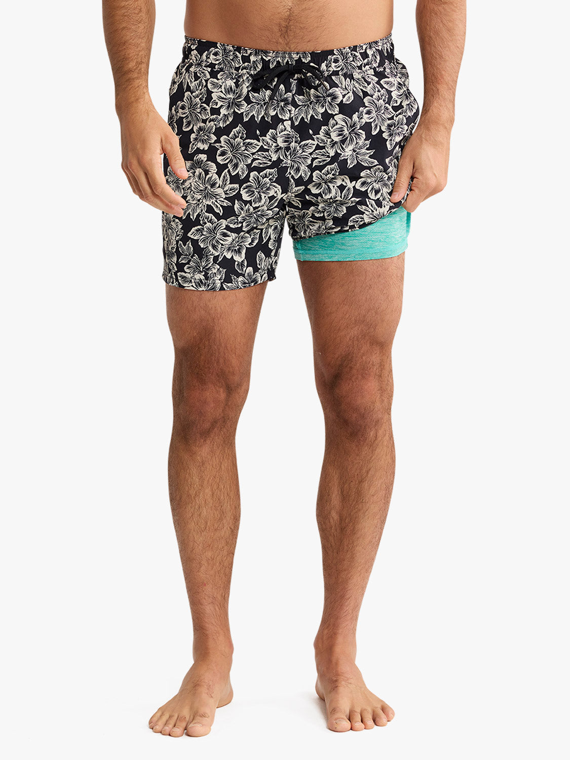 Man wearing black swim trunks with white hibiscus floral print and turquoise side panel.
