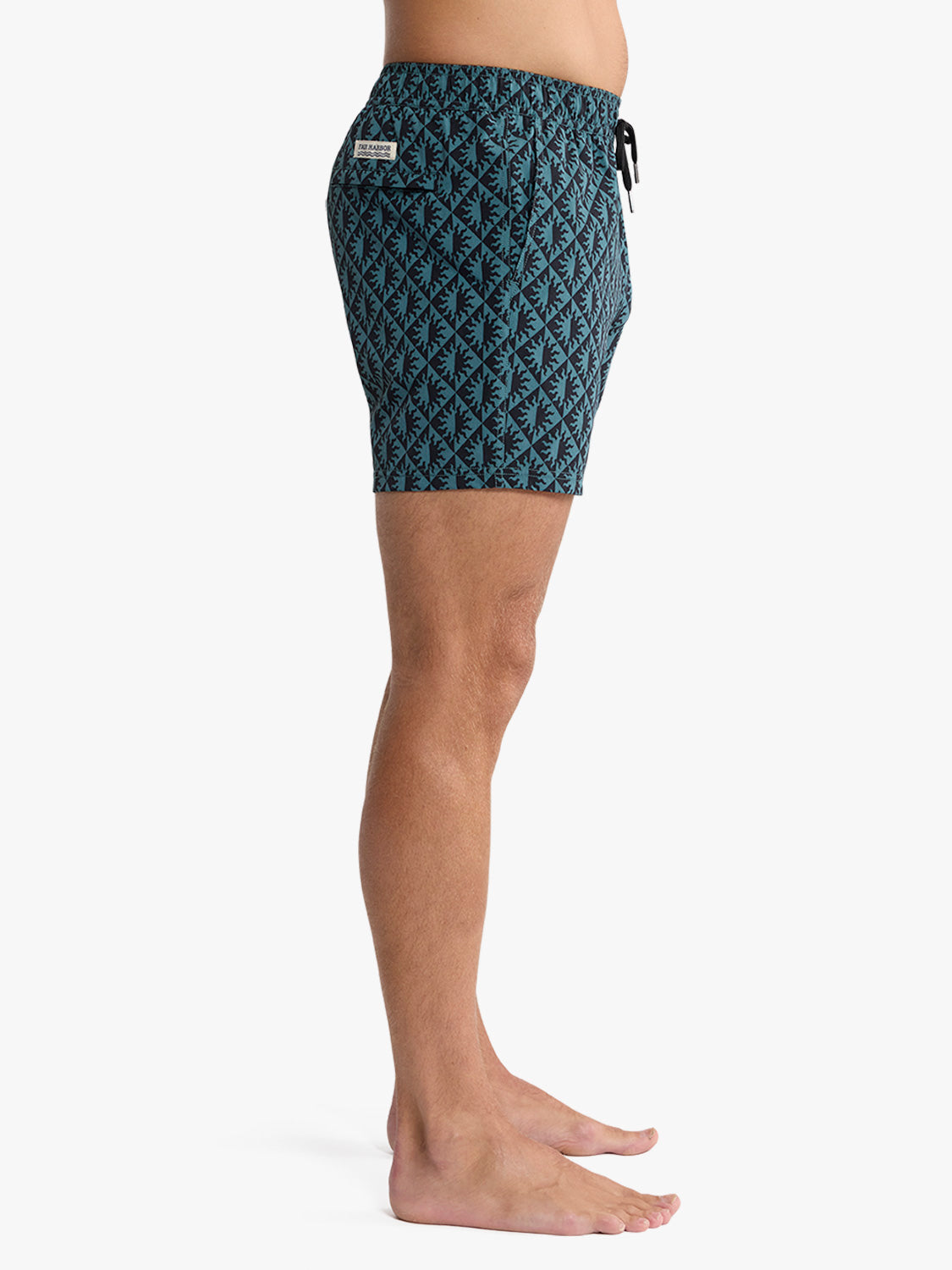Man wearing teal and black geometric patterned swim trunk with drawstring closure.