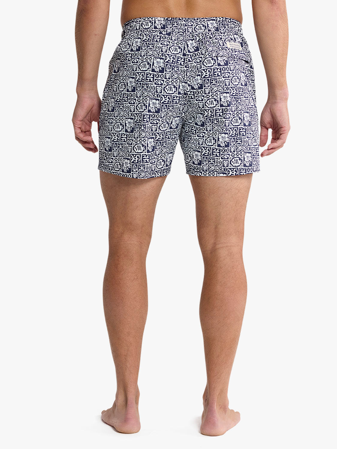 Man wearing navy and white patterned swim trunks with geometric tile design shown from behind.