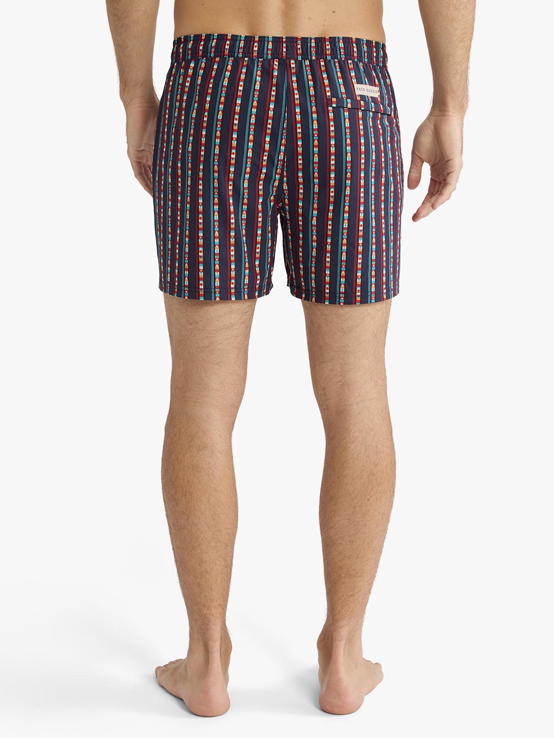 Man wearing navy swim trunks with red and teal vertical stripe pattern and elastic waistband.