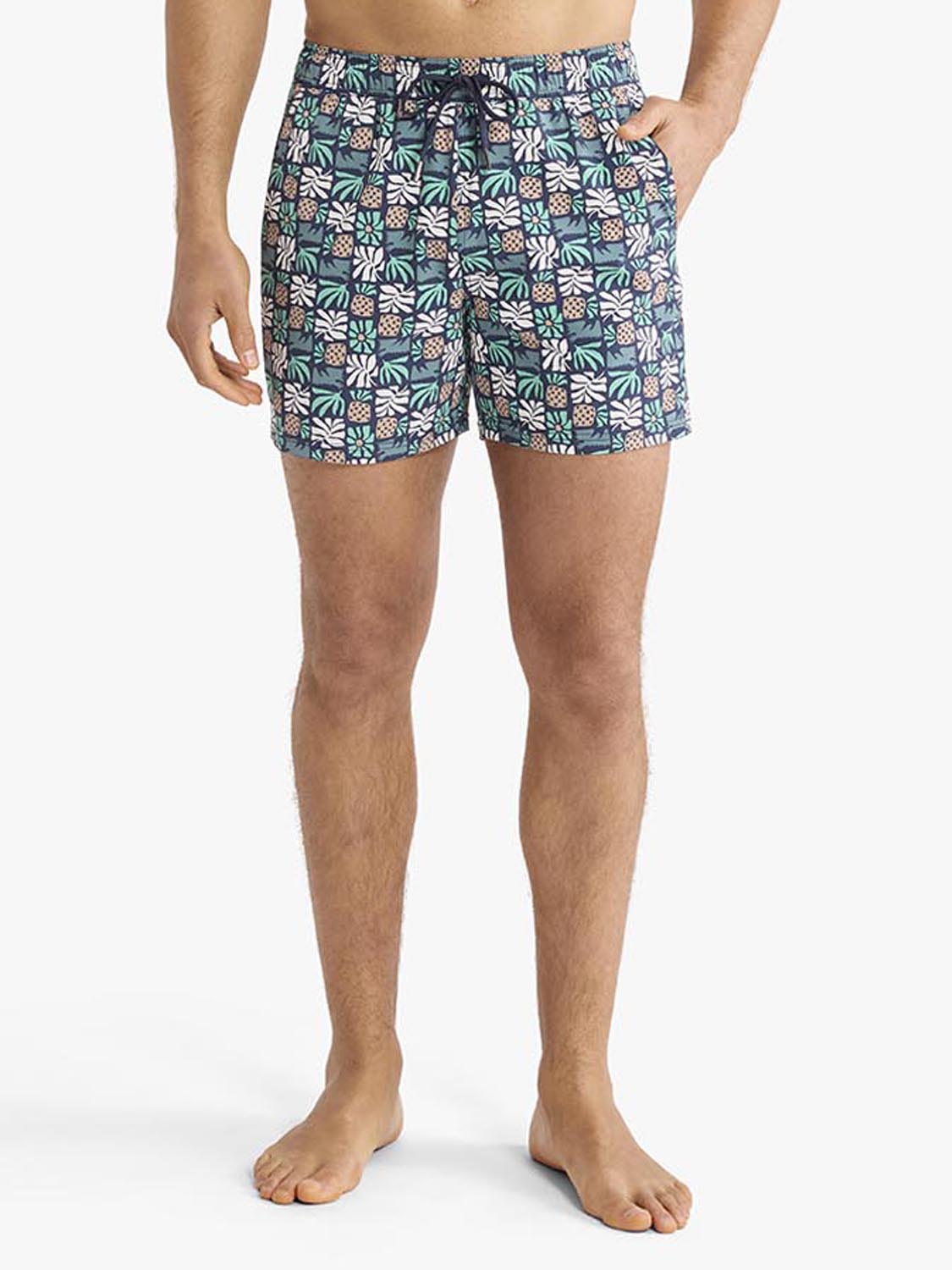 Man wearing navy swim trunks with white and coral palm tile pattern and side pockets.