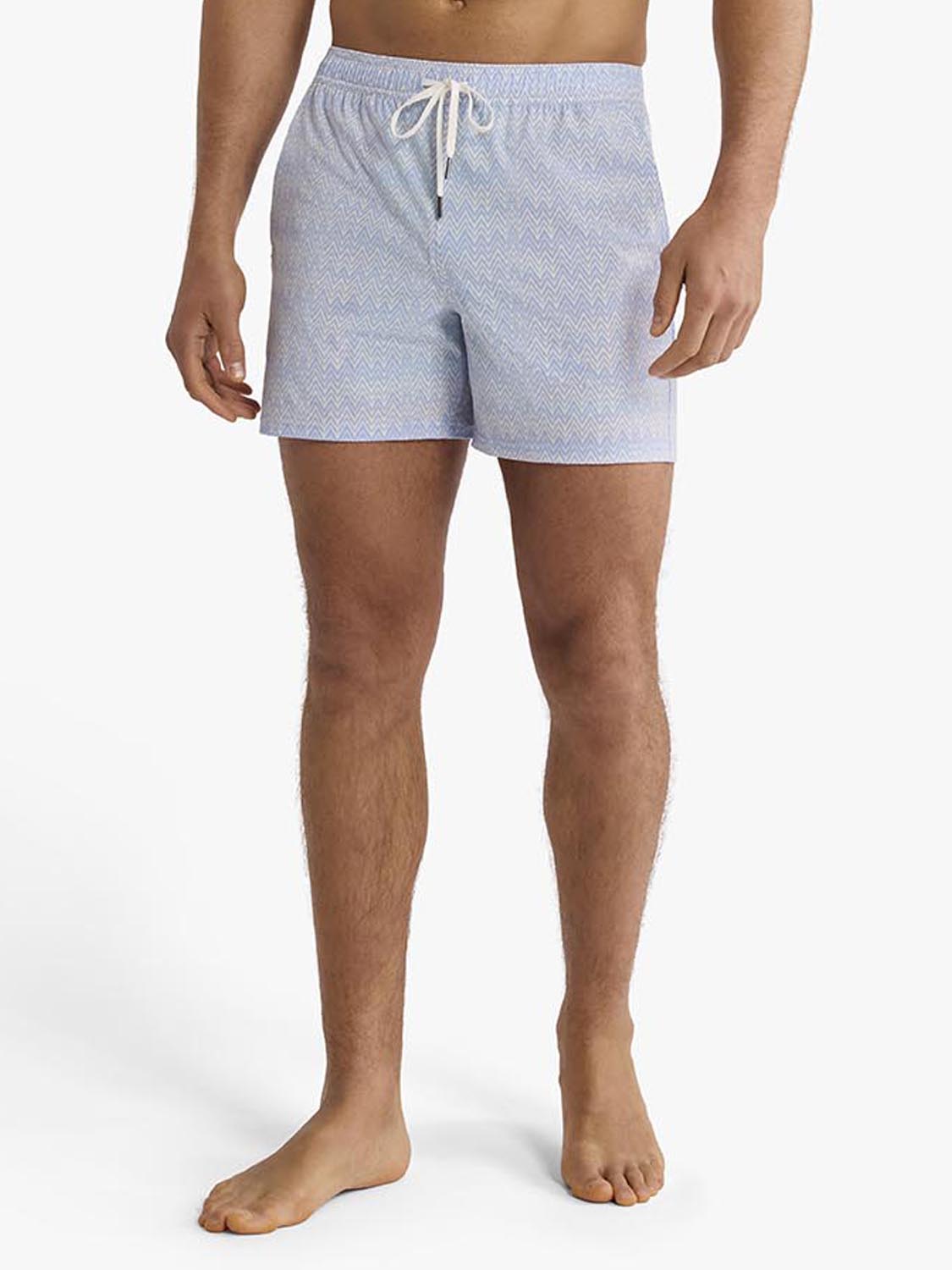Man wearing light blue textured swim trunks with a drawstring waist and chevron pattern.