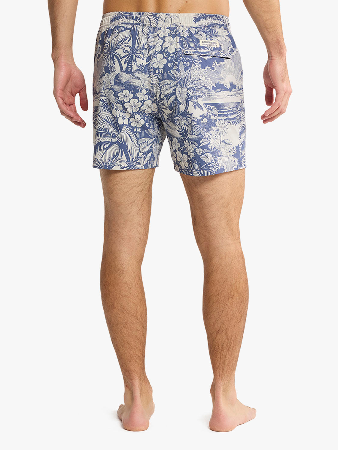 Man wearing navy and cream tropical print swim trunks with palm and floral patterns.