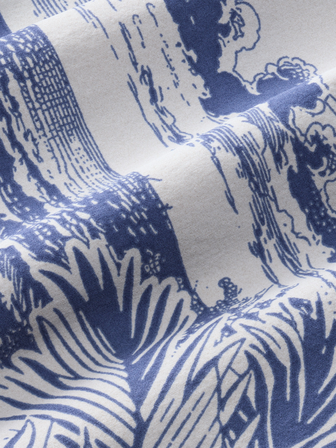 Close-up of blue and white fabric featuring palm leaf and botanical motifs in detailed line work pattern.