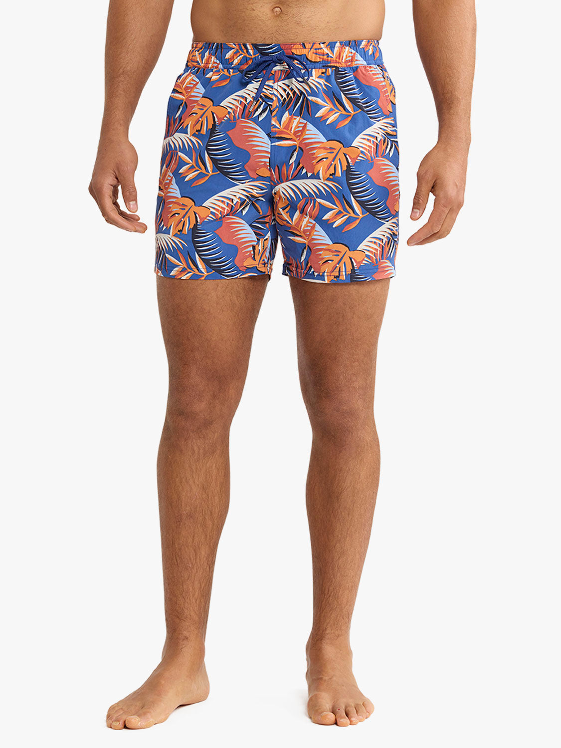Man wearing blue swim trunk with orange and coral palm leaf pattern throughout.