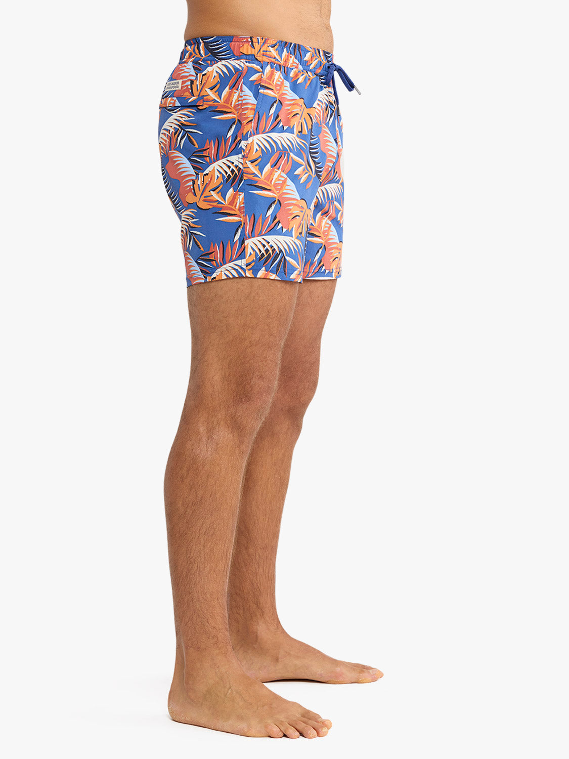 Man wearing blue swim trunks with orange and white palm leaf print and drawstring waist.