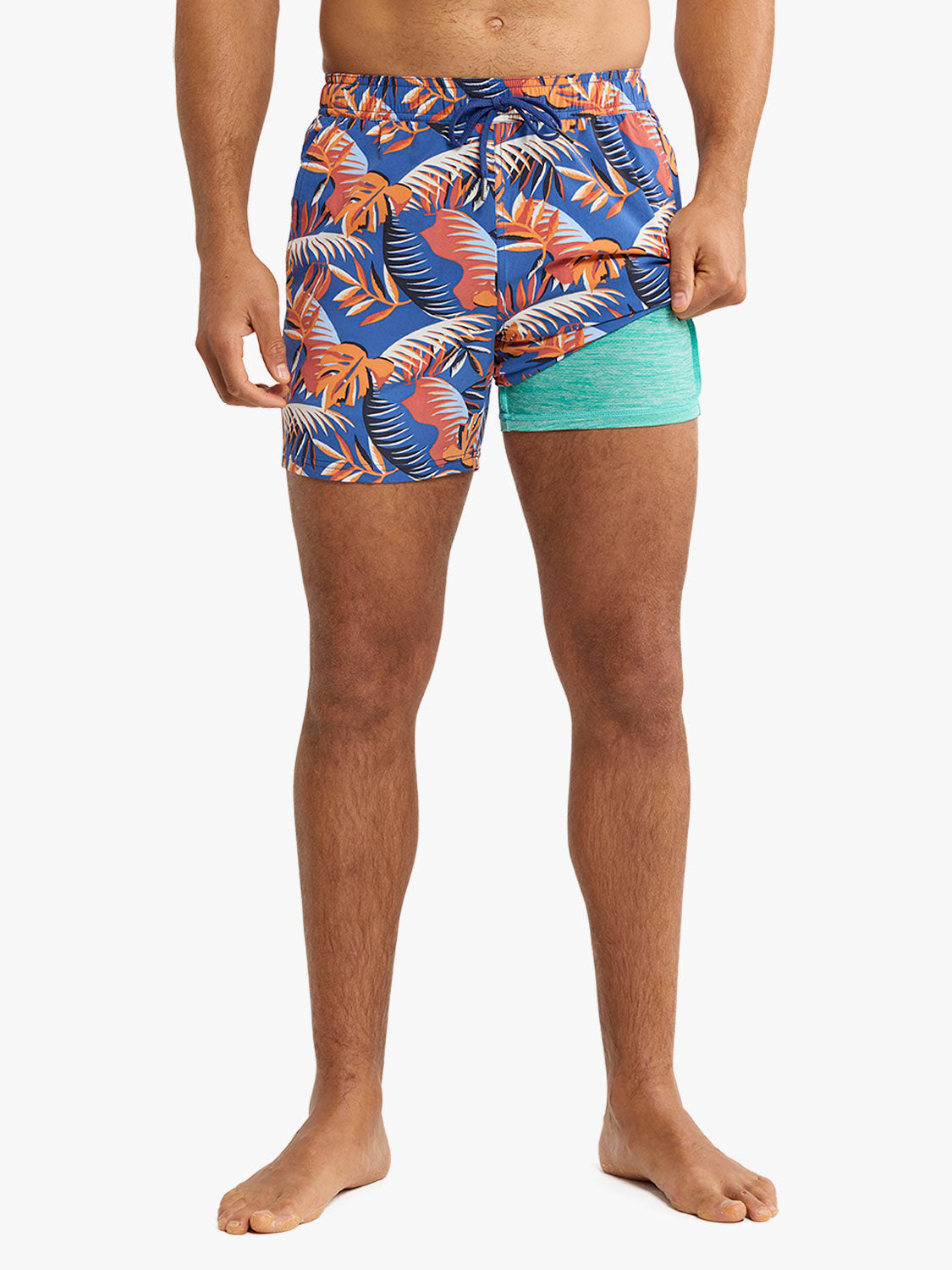 Man wearing blue swim trunks with orange and white palm leaf pattern and turquoise inner shorts.