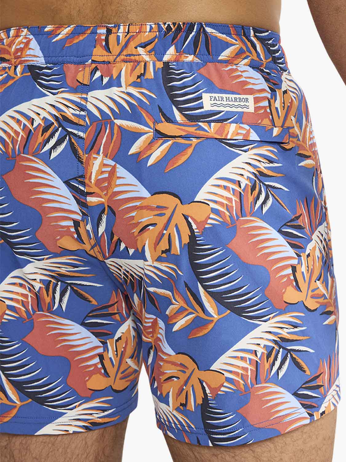 Blue swim trunks with orange, red, and white tropical palm leaf print pattern displayed on model.