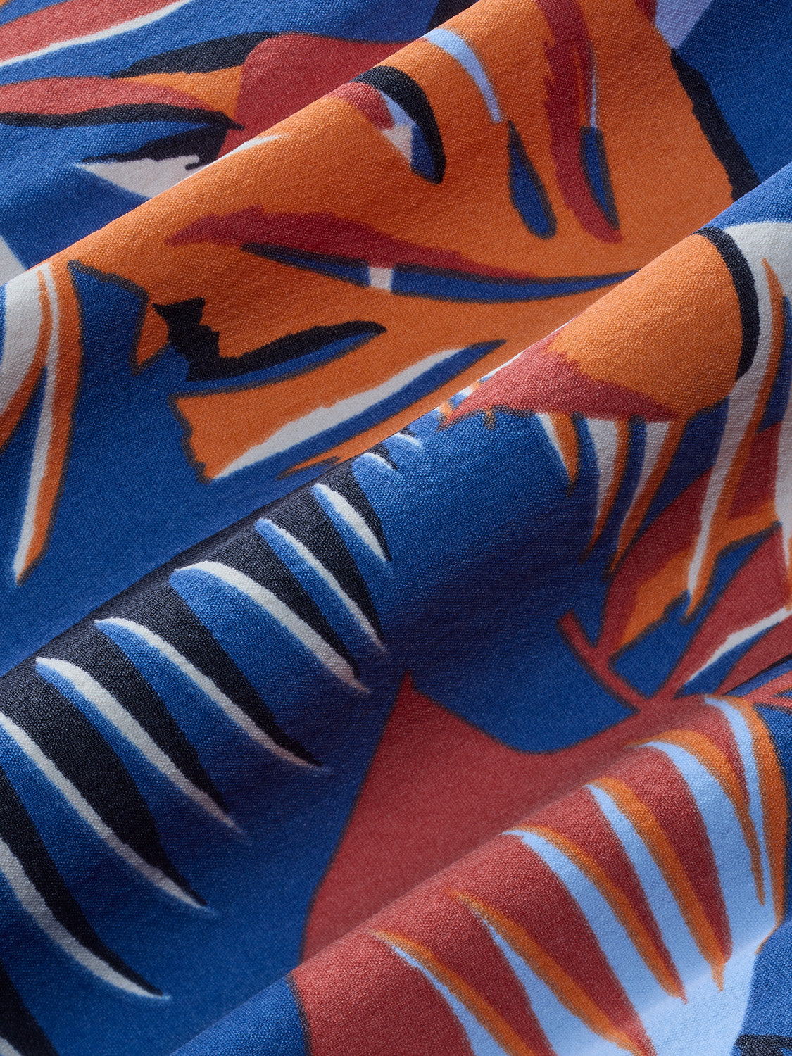 Close-up of folded fabric showing orange, blue, burgundy, and white striped palm leaf pattern design.