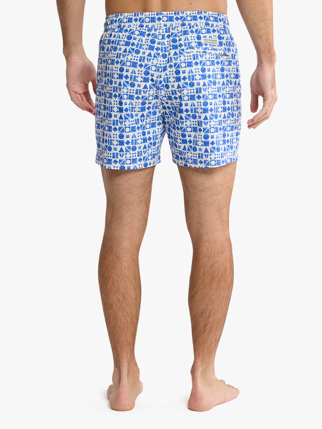 Man wearing blue and white geometric patterned swim shorts from behind, standing barefoot.