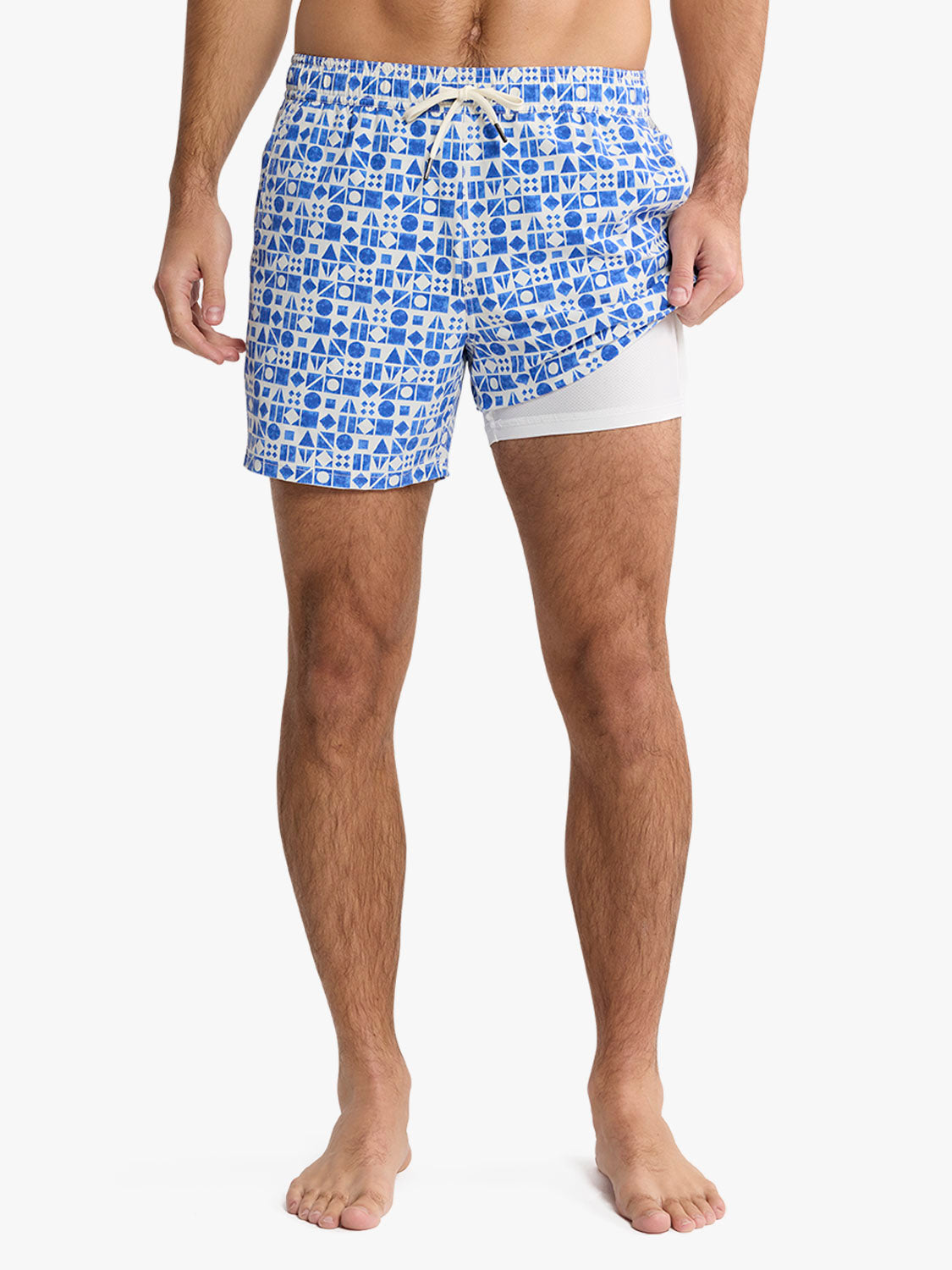 Man wearing blue and white geometric patterned swim trunks with white mesh lining underneath.